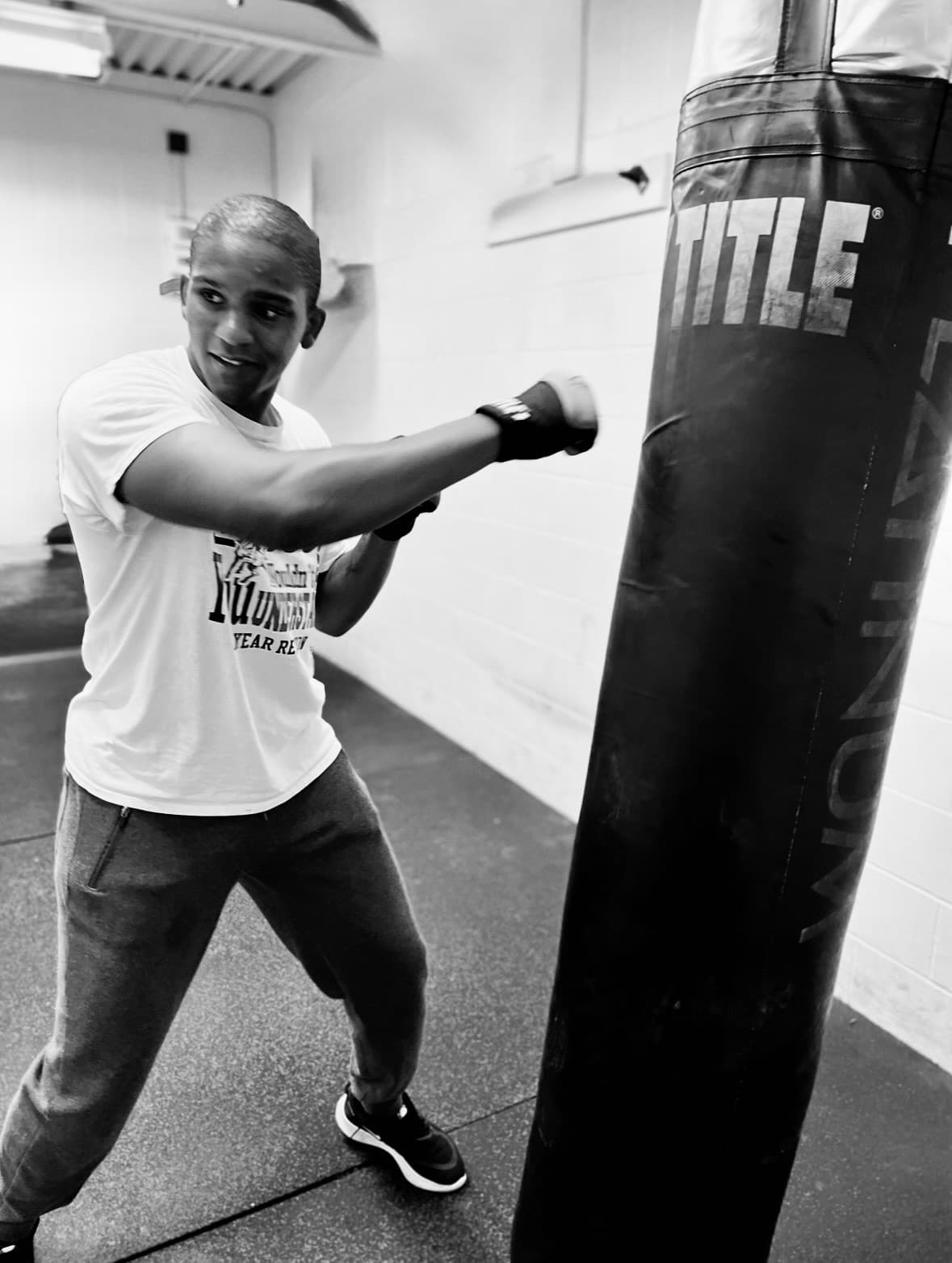 Focused person in a white t-shirt punches a TITLE heavy bag in a gym.